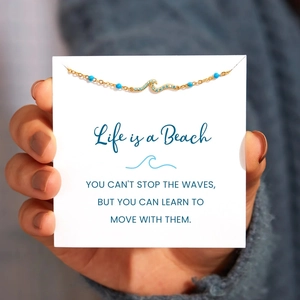 Gold ocean wave necklace with blue crystals and beads on a motivational display card
