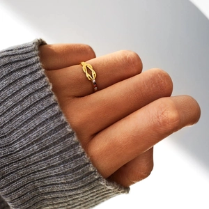 Elegant gold knot ring with four colorful gemstones worn on hand over gray knitwear