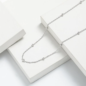 Detailed view of silver minimalist bead chain necklace on geometric display stands