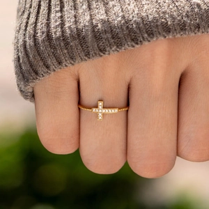 Bague croix dorée élégante ornée de zircons portée par un mannequin avec un pull en maille