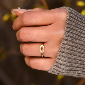 Close-up of gold knot ring with white blue and red birthstones worn on finger