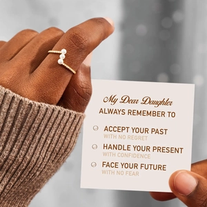 Detail of gold ring with three white pearls shown with a sentimental gift card for daughter