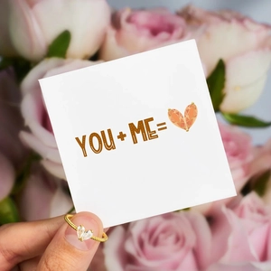 Close-up of golden rope band ring with dual heart-shaped crystals on a romantic card