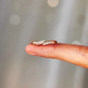 Macro shot of rose gold wave ring with sparkling pavé diamonds on a finger