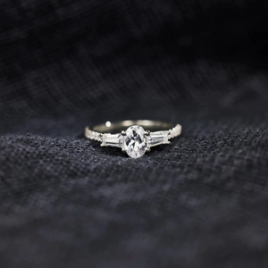 Macro shot of oval cut center stone ring with baguette side diamonds and pavé band