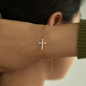 Macro detail of gold cross bracelet featuring sparkling round cut white zircons