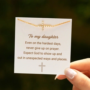 Close-up of gold cross pendant with cubic zirconia on inspirational gift card for daughter
