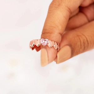Détail d'une pierre précieuse cœur rose sur un anneau en cœurs ajourés or rose