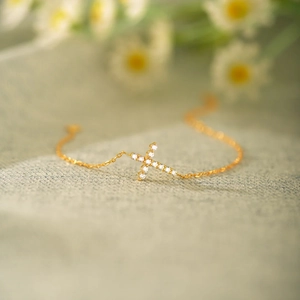 Macro detail of gold cross bracelet with shimmering zircon stones on soft textile