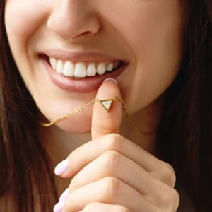Close-up of a minimalist gold triangle opal necklace held between fingertips