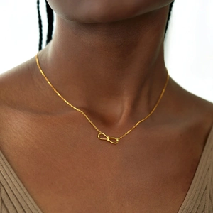 Polished gold S925 sterling silver infinity knot necklace worn on a woman's collarbone