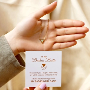 Close-up of gold triangle opal necklace held by hand with friendship gift card