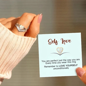 Close-up of S925 sterling silver opal heart ring worn with a Self Love message card