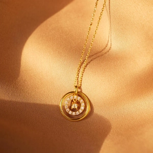 Détail du collier à double cercle doré avec pavage de pierres et pendentif diamant central