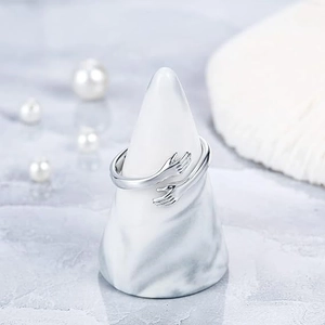 Detail shot of silver hugging hands ring on a marble display stand with elegant pearls