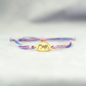 Macro detail of hand-woven colorful cord bracelet with engraved golden promise charm