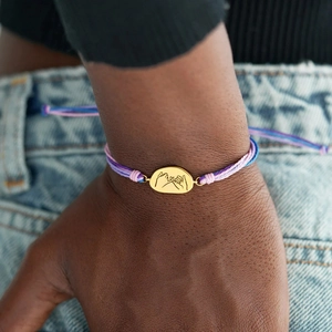 Macro detail of multicolored braided cord bracelet featuring a gold pinky swear charm