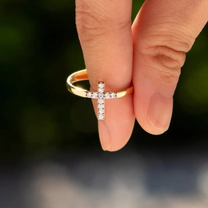 Close-up of gold cross ring with pavé crystals on a finger, elegant fashion jewelry