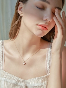 Close-up of a gold heart pendant necklace with white opal and daisy stud earrings on model