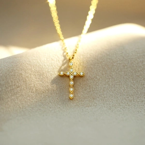 Elegant gold infinity cross pendant necklace with clear crystals on a beige display stand