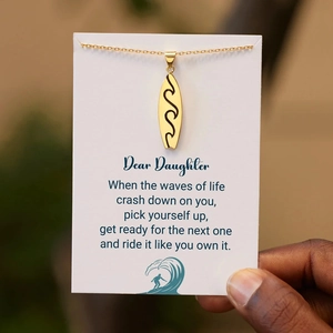 Detailed view of wave-engraved surfboard pendant on gift card for daughter