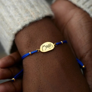 Bracelet tressé bleu fait main avec breloque dorée Pinky Swear porté sur le poignet