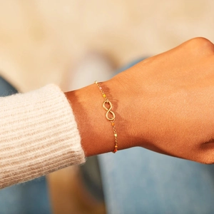 Golden infinity bracelet with colorful enamel beads on a woman's wrist with a cozy sweater