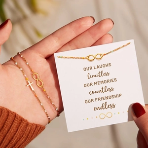Close-up of gold infinity and cross charm bracelet on wrist with a friendship card