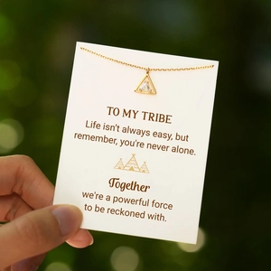 Gold triangle necklace with zircon on a Tribe card held against a blurry green background