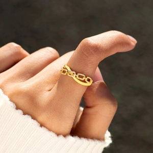 Anello a catena dorata con zirconi pavé su mano femminile su sfondo scuro elegante