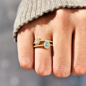 Double layered gold ring with oval blue and white birthstones worn on a finger