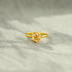 Macro d'une bague nœud dorée ornée de pierres scintillantes sur tissu texturé