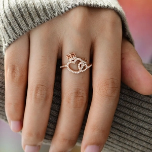 Rose gold interlocking heart ring with crown detail worn on finger over gray sweater
