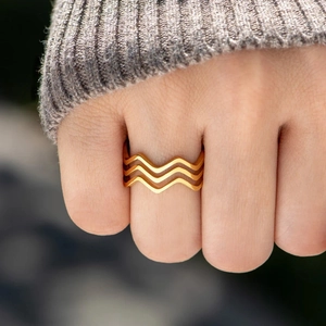 Gros plan d'une bague triple vague dorée au doigt avec un fond de chandail en tricot doux