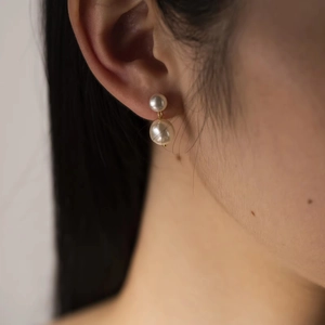 Elegant double white pearl drop earrings with gold finish on model's ear