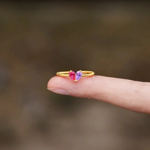 Golden rope band ring with teardrop birthstones forming a heart on a finger tip
