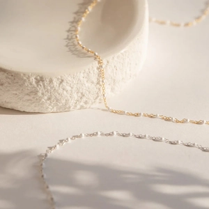 Close-up of gold and silver minimalist beaded necklaces on a natural stone display