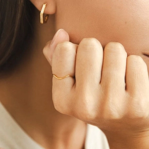 Minimalist gold wavy stacking ring worn by model with matching gold hexagon hoop earrings
