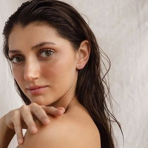 Close-up of model wearing dainty s925 silver four-leaf clover flower stud earrings with blue stones