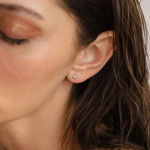 Close-up of small S925 silver clover stud earrings with opal petals on earlobe