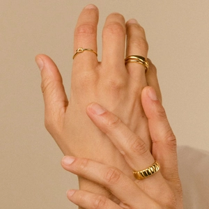 Detail of stacked gold knot rings and ribbed band on finger with elegant warm lighting