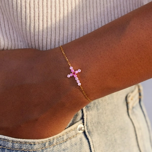Gros plan d'un bracelet croix en zircon rose dégradé et chaîne dorée au poignet