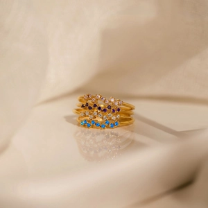 Set of four stackable gold rings featuring colorful birthstones on a white fabric surface