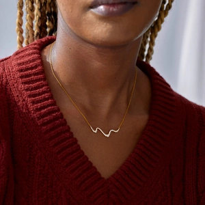 Close-up of a wavy gold vermeil necklace with pavé zircons worn on a red knit sweater