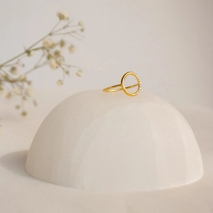 Détail d'une bague en argent s925 doré avec cercle de cristaux sur support blanc