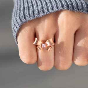 Rose gold bow ring with pink square gemstone on frosted surface worn on hand