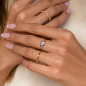 Three-piece gold stacked ring set featuring purple rectangular stones on female hand