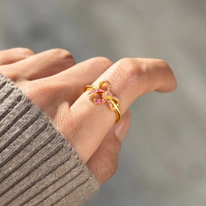 Elegant gold bow ring with pink zircon stones worn on a grey knit sweater background