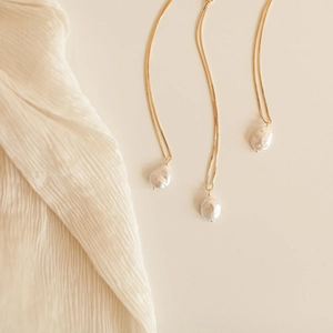 Three gold s925 silver necklaces with baroque freshwater pearls on beige silk fabric