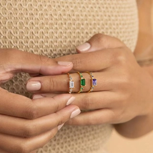 Three elegant gold-plated rings with emerald-cut stones in white, green, and purple